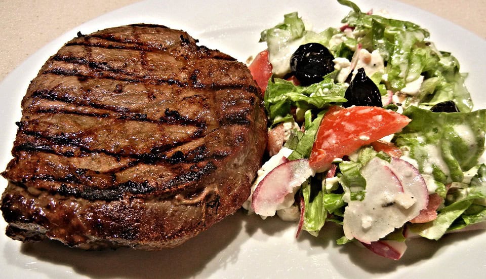 Grilled steak with grill marks next to a fresh garden salad on a plate