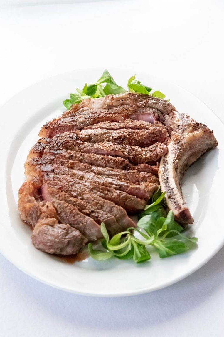 Sliced rib steak on plate with greens.