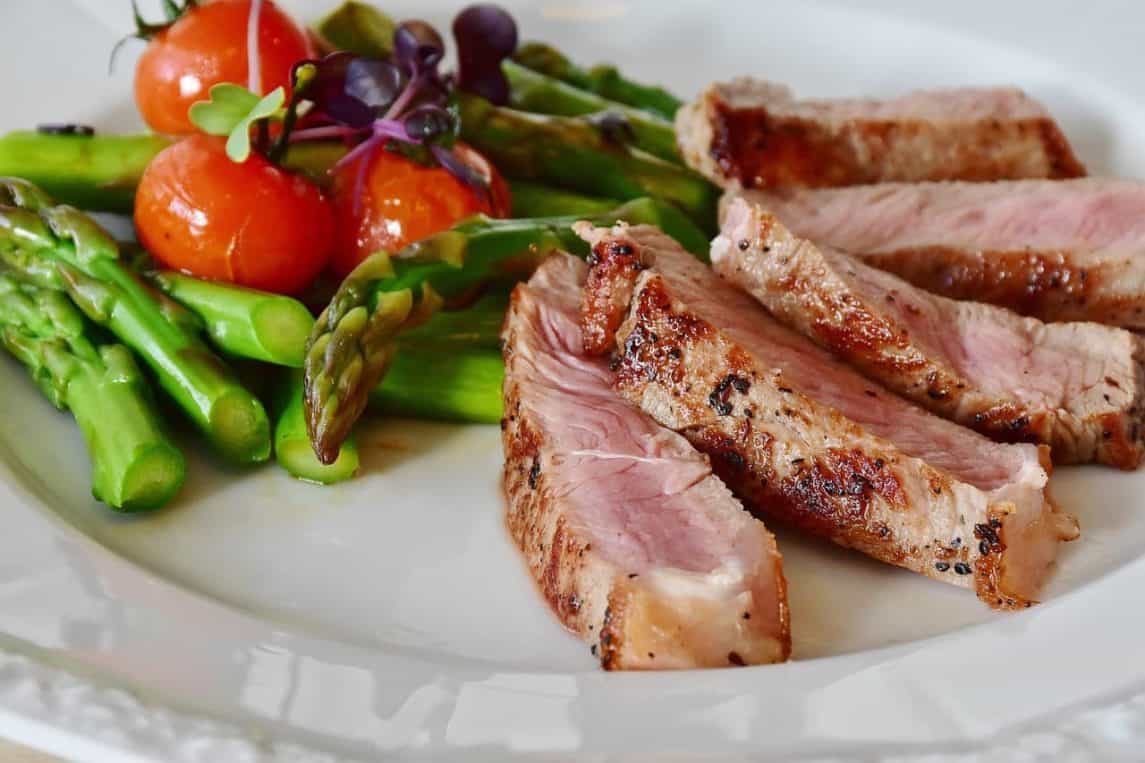 Sliced steak with asparagus and tomatoes on a plate.