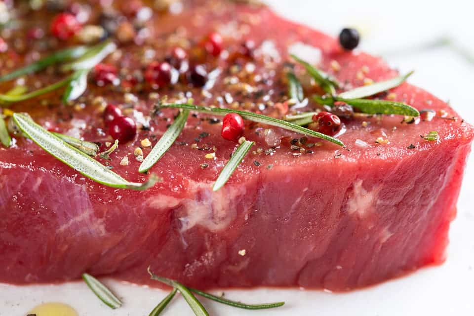 Raw steak seasoned with pepper, salt, and rosemary